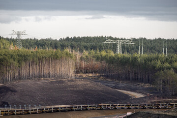 Trees of a forest next to an open cast mine. The pine trees get cleared to exploit the lignite deposit. Humans destroy the nature for fossil fuels like brown coal. The global warming is a result.