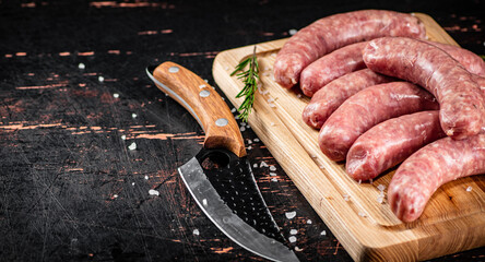 Raw sausages on a cutting board with a knife and rosemary. 