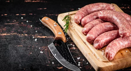 Raw sausages on a cutting board with a knife and rosemary.  © Artem Shadrin