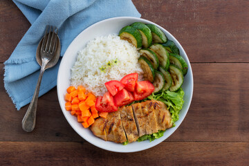 Healthy food grilled chicken has rice zucchini carrot tomato in plate on wood table.