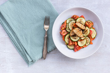 Healthy food grilled chicken salad has zucchini carrot tomato in white bowl on wood background.
