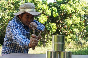 Asian man holds slingshot to play  shooting game, aim to shoot the  cans in forest. Concept,...