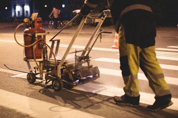 Process of making new road surface markings with line striping machine, workers improve city infrastructure, demarcation marking of pedestrian crossing with hot melted paint on asphalt pavement