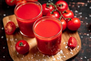 Tomato juice in glasses on a wooden cutting board. 