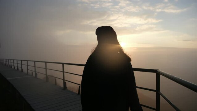 Silhouette image of a female traveler standing on wooden bridge and watching sunrise in the morning