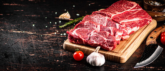Raw beef on a wooden cutting board with rosemary.