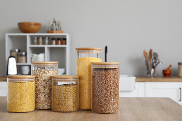 Glass jars with different cereals on wooden table in kitchen