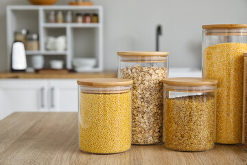 Glass jars with different cereals on wooden table in kitchen, closeup