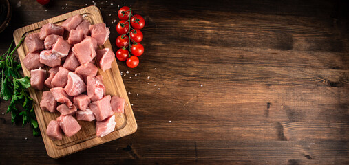 Pieces of raw pork on a cutting board with parsley and tomatoes. 