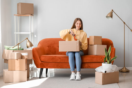 Young woman taping cardboard box in living room on moving day