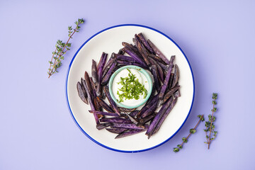 Plate with sticks of fried purple potatoes, sauce and thyme on color background
