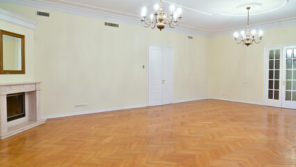A huge empty room without furniture with laminate flooring and high ceilings and chandeliers.