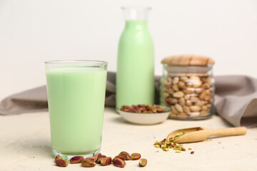 Glass of tasty pistachio milk and kernels on light table