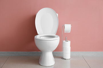 Obraz na płótnie Canvas Ceramic toilet bowl and paper rolls near pink wall