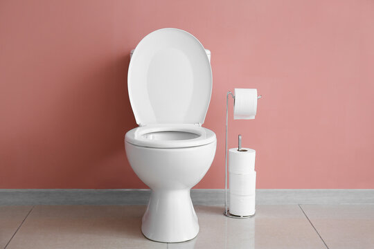 Ceramic toilet bowl and paper rolls near pink wall