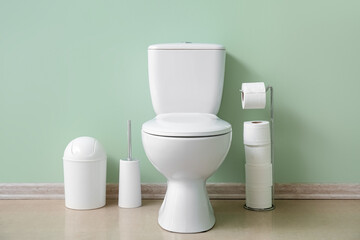 Ceramic toilet bowl, bin and paper rolls near green wall