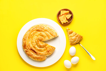 Plate with delicious cheese pie and eggs on yellow background