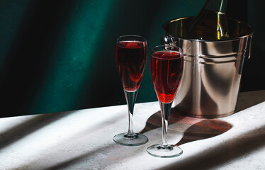 Kir Royale alcoholic cocktail with blackcurrant liqueur, prosecco and cocktail cherry. Dark green background, hard light and shadow pattern