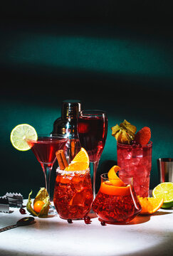 Red alcoholic cocktails set: kir royale, negroni, boulevardier, cosmopolitan, sea breeze with fruits and citrus. Bar tools. Dark green background, hard light and shadow pattern