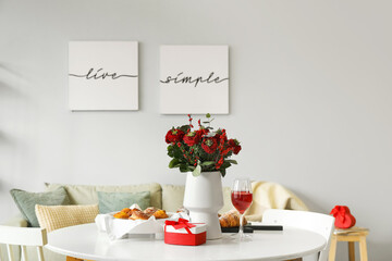Vase with flowers, pastries, glasses of wine and gift for Valentine's Day on dining table in room