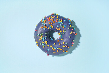 Delicious glazed donut with colorful sprinkles on blue background