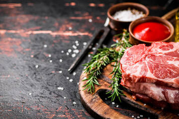 Raw pork steak on a wooden cutting board with tomato sauce,rosemary and spices. 
