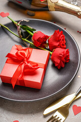 Table setting for Valentine's Day with gift and red roses on table
