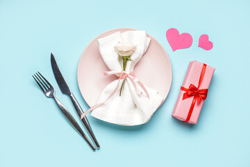 Table setting for Valentine's Day with rose, gift and hearts on light blue background