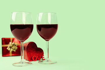Glasses of wine, word LOVE and gifts on green background. Valentine's Day Celebration