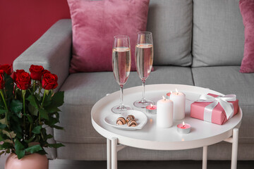 Burning candles, glasses of champagne, candies and gift for Valentine's Day on table in living room
