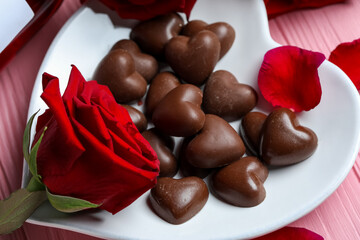 Heart-shaped plate with chocolate candies, bottle of wine and rose flower on pink wooden background. Valentine's Day celebration