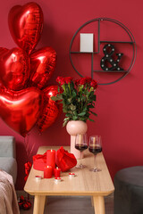 Burning candles, wine, vase with roses and gifts for Valentine's Day on table in living room