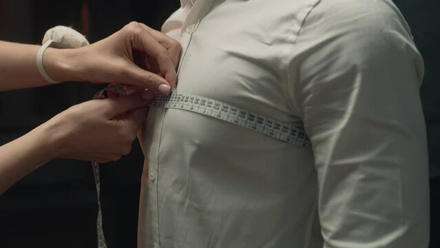 Cinematic shot of female tailor takes measurements of client for wedding or business suit shirt. Work in luxury designer atelier or tailoring studio. Concept of fashion, handmade and couturier.