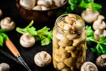 Pickled mushrooms in a jar with greens on a stone board. 