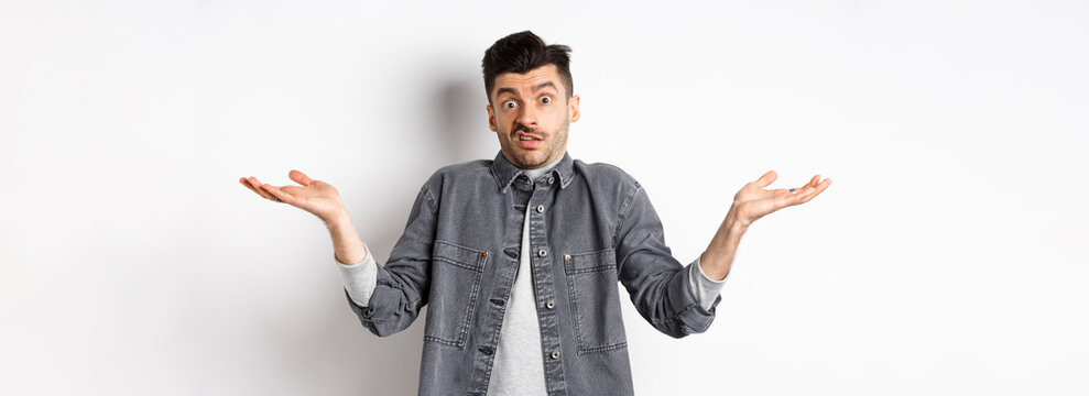 I Dont Know. Clueless Young Man Shrugging And Looking Confused, Have Nothing To Say, Standing Unaware On White Background