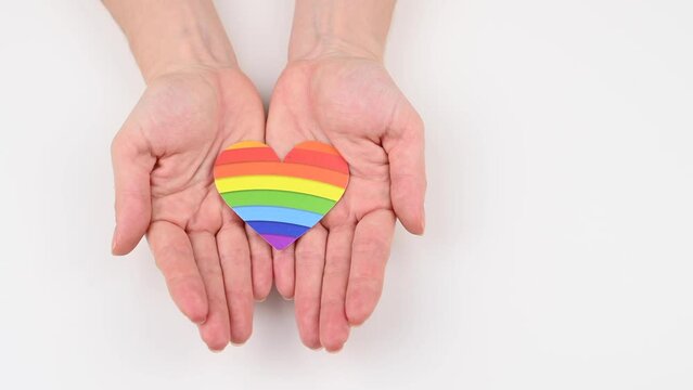 A woman opens her palms and shows a rainbow heart on a white background. 