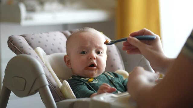 baby newborn eats. happy family dream weaning concept. dirty mess baby boy eating vegetables. baby son eats indoors on a feeding chair dirty face. naughty dirty babe indulges while feeding