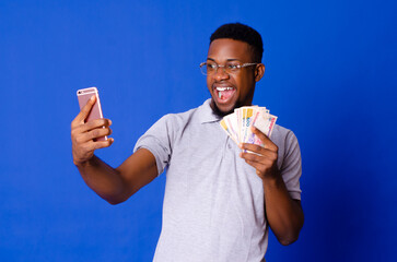 Young handsome African man on glasses taking selfie with his mobile phone and holding cash, on an isolated background