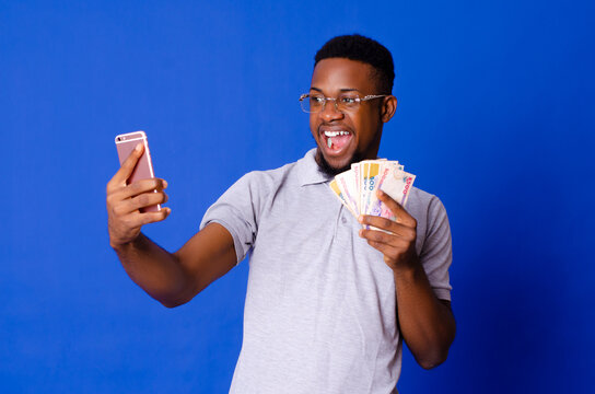 Young handsome African man on glasses taking selfie with his mobile phone and holding cash, on an isolated background