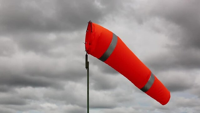 Windsock indicator of wind on tank chemical cone indicating wind direction and force. Horizontally flying windsock (wind vane) with cloud sky in the background.