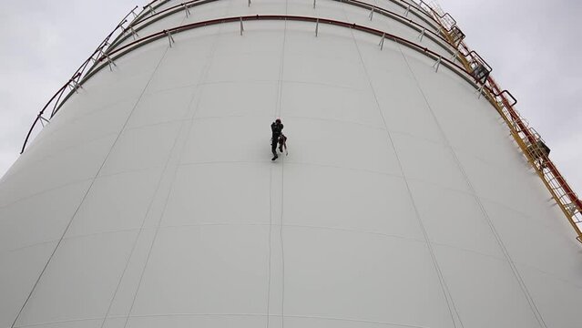 Male worker down height tank shell plate rope ladder  access safety inspection of thickness storage tank gas propane.
