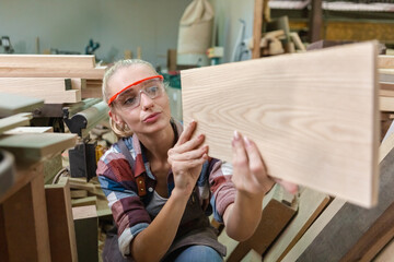 young carpenter woman wear uniform and goggles choose the size and quality wood used for work. craftsman professional concept. woodworking industry.