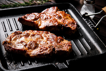 Cooked pork steak in a frying pan grilled with rosemary. 