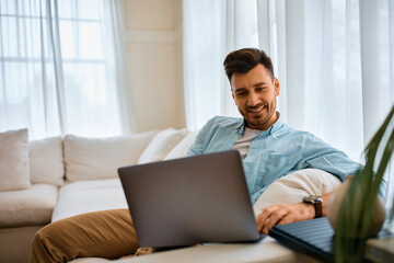 Happy man surfing the net on laptop at home.