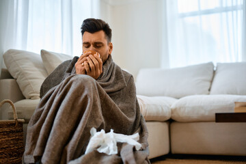 Fototapeta premium Sick man wrapped in blanket having cup of warm tea at home.