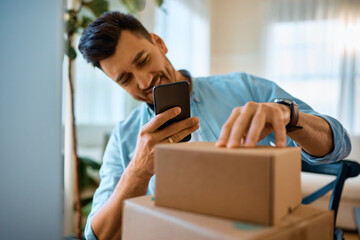 Happy man scanning code on cardboard boxes at home.