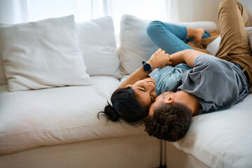 Happy couple lying embraced on sofa at home.