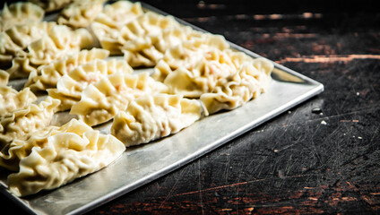 Raw dumplings gyoza on a baking sheet. Against a dark background.