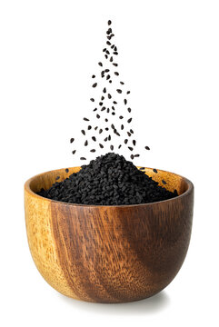 black cumin seeds falling in wooden bowl isolated on white