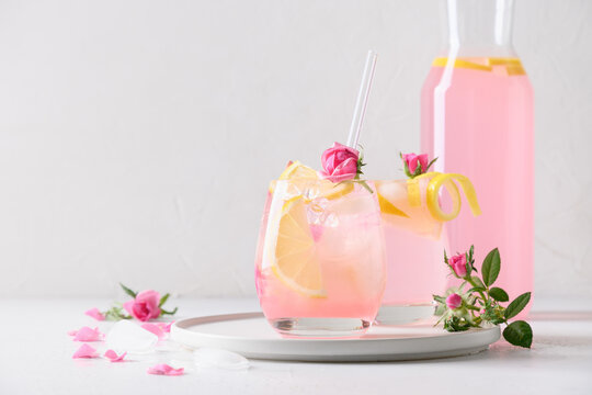 Pouring pink alcoholic cocktail with rose flowers on white background.